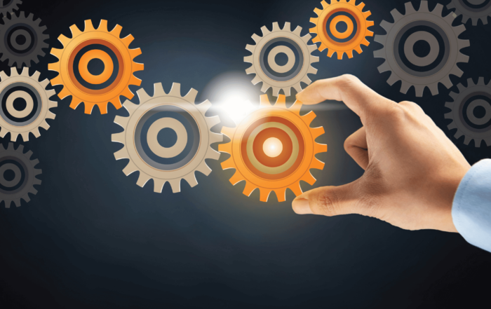 Orange and tan gears on a dark background with a hand reaching out to turn them.
